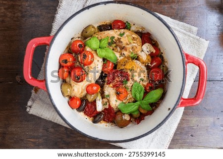 A rustic pot filled with cooked chicken breasts, cherry tomatoes, olives, garlic, and fresh basil. The dish is colorful and garnished with herbs.