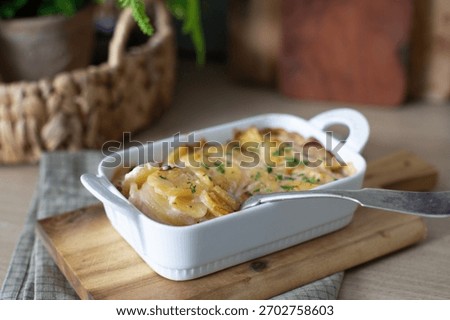 Rustic potato gratin featuring thinly sliced potatoes layered with cream and cheese, baked until bubbly and golden. Photographed in natural light on a wooden board for a cozy home-cooked feel.