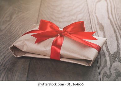 rustic present box with red ribbon on wood table, vintage toned photo