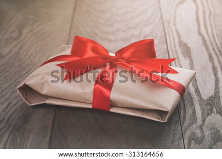 rustic present box with red ribbon on wood table, vintage toned photo