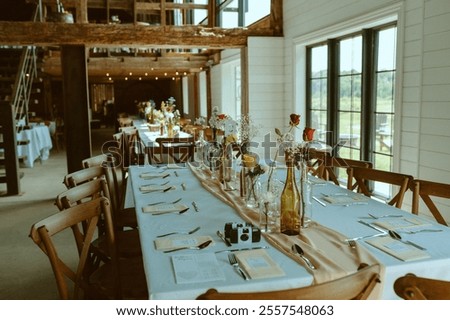 A rustic reception table adorned with wildflowers in glass bottles, a soft neutral runner, and vintage accents. Wooden chairs and natural light create a charming, romantic wedding ambiance.
