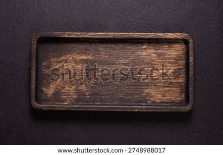 Rustic rectangular wooden board with rich dark brown grain on a gritty black surface, ideal for food presentation, product display, or minimal culinary background space