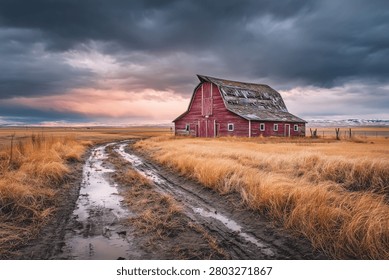A rustic red barn in a vast field under dramatic cloudy skies with a muddy path leading to it, capturing rural charm and tranquility.