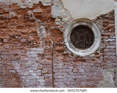 Rustic Red Brick Wall with Round Window - Close-up texture of an old, damaged red brick and plaster wall with a circular stone-framed window (oculus) and decorative rusted metal grating.