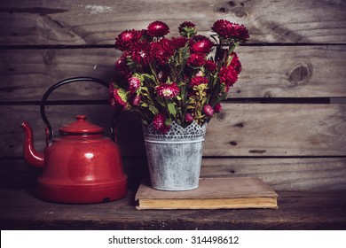 Rustic Red Flowers In A Can Vase And An Old Enamel Kettle On An Old Vintage Wooden Board Background. Country Kitchen Decor.