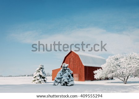A rustic red Ohio barn covered in fresh snow with a bright blue sky background.