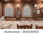 Rustic restaurant dining area featuring exposed brick wall with twin arched niches, ornate gold baroque mirror, wooden chairs, long table set with white linens and glassware under warm sconce lighting