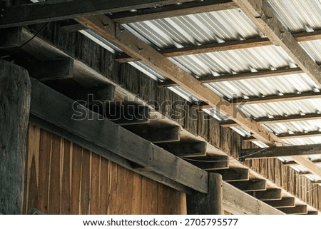 rustic roof structure. The foreground features smooth, warm-toned vertical wooden planks and stepped timber eaves, providing a strong contrast to the bright, angular lines of the corrugated metal roof