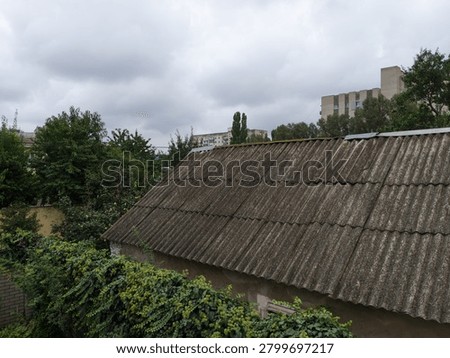 A rustic roof under a cloudy sky with surrounding greenery and urban buildings.