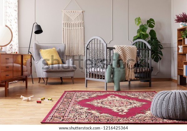 Rustic rug in stylish baby bedroom\
with grey and vintage furniture, real photo with copy\
space