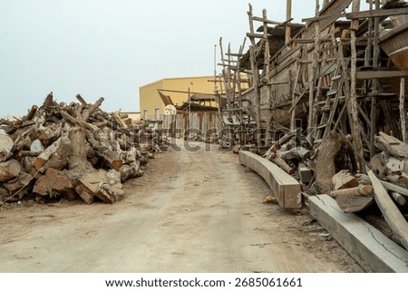 A rustic scene depicting a path through a shipbuilding yard filled with stacked logs and wooden scaffolding.
