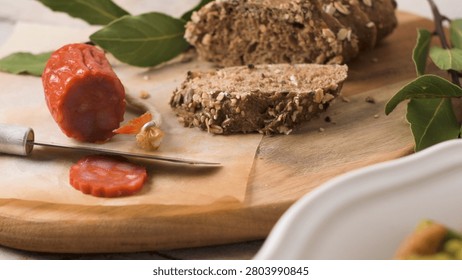 A rustic scene features sliced chourico sausage alongside rustic multigrain bread on a wooden board. Soft natural lighting enhances the varied textures of the grains and cured meat.