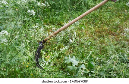 Rustic scythe on a background of green grass. The male hand holds a scythe, a sharp scythe mows the grass