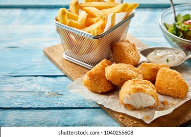 Rustic serving of crumbed fried kibbeling or bite sized portions of codfish fillet served with tartare sauce and a wire basket of French fries on rustic blue wood table - Powered by Shutterstock