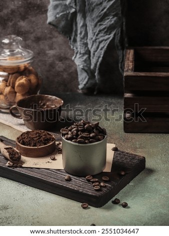 A rustic setup featuring whole coffee beans and ground coffee placed on a wooden board, accompanied by a jar of biscuits in the background. Perfect for conveying warmth and coziness.
