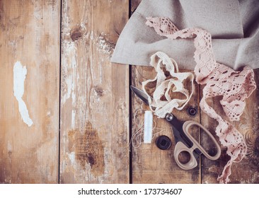 Rustic sewing background: scissors, thread, fabric and lace on an old wooden board, hand-made and crafts, close up