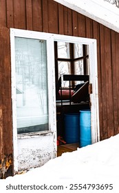 A rustic ski cabin with a partially opened door, revealing barrels inside. Surrounded by a winter landscape, the image captures the essence of a snowy ski resort environment.