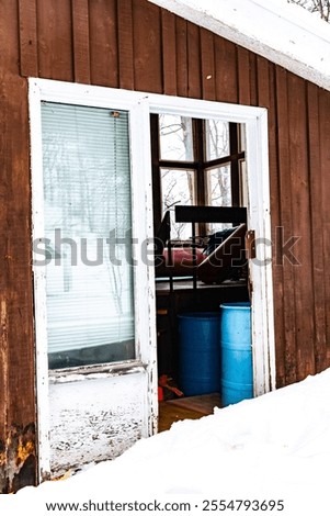 A rustic ski cabin with a partially opened door, revealing barrels inside. Surrounded by a winter landscape, the image captures the essence of a snowy ski resort environment.