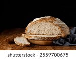 Rustic sourdough bread with cut slices on a wooden table on black background with free space for text