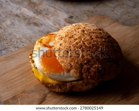 Rustic sourdough bread roll sandwich with sunny side up fried egg and melted cheese on wooden cutting board, homemade breakfast brunch