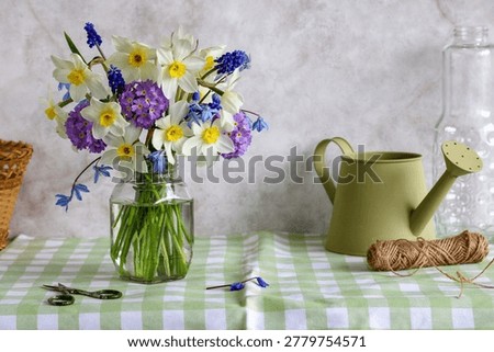Rustic spring still life with fresh wildflowers in glass jar, green watering can, twine and scissors on farmhouse table