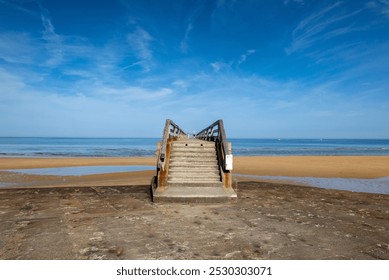 Rustic staircase leading to the sandy shores and tranquil blue waters of Normandy, France, under a clear sky, capturing the serene beauty of the coastline. - Powered by Shutterstock