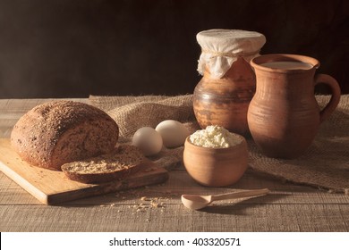 Rustic still life. The morning sun from the window. Country breakfast. Jug with milk, black bread, cheese, eggs, a wooden table. - Powered by Shutterstock