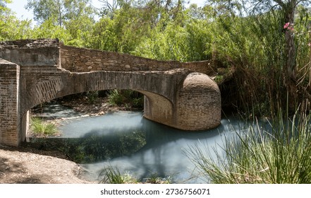 A rustic stone bridge over a calm river surrounded by lush greenery
