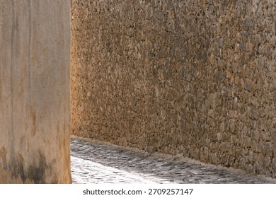Rustic stone wall and cobblestone pathway in sunlit alley.