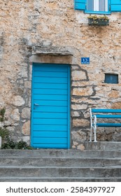 Rustic stone wall featuring a vibrant blue door and a matching bench, exuding charm and serenity. Solta, Croatia.