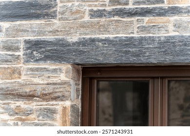 A rustic stone wall with a modern window frame, showcasing a blend of old and new architectural styles.