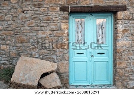 Rustic stone wall with an old turquoise wooden door, typical of Mediterranean architecture. Traditional village house exterior with vintage charm. Horizontal close-up.