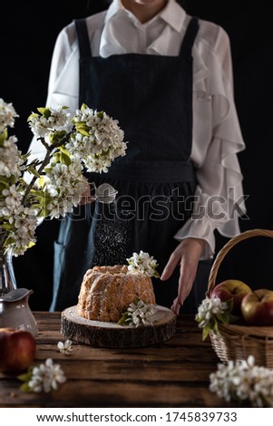 Rustic style apple bundt cake with powdered sugar. Woman sprinkles icing sugar throug sieve on apple cake