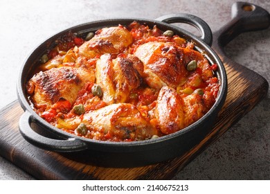 Rustic style chicken baked with a sauce of tomatoes, peppers, onions and garlic close-up in a frying pan on a cutting board. horizontal