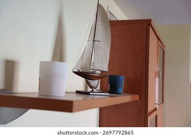 Rustic style shelf with tiny sailing vessel, Gentle sunlight illuminates cozy shelf featuring miniature boat and vintage ceramics in muted tones