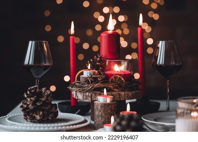 Rustic table decor for Christmas or New Year family dinner. Centrepiece with red candle, dry orange, cone, cinnamon, anise. Zero waste eco-friendly home. Cozy atmosphere, dark background. Close up