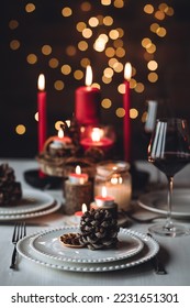 Rustic table decor for Christmas or New Year family dinner. Centrepiece with red candle, dry orange, cone, cinnamon, anise. Zero waste eco-friendly home. Cozy atmosphere, dark background. Close up