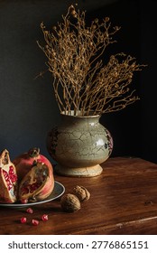 Rustic table setting with cracked ceramic vase containing dried branches next to open pomegranate.