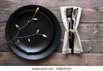 Rustic table setting. Elegant empty black plate, cutlery on linen napkin and natural tree branch on rustic planked wood. High quality photo