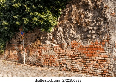 Rustic texture of an old brick wall merging with rough stone and overgrown green ivy. Urban architectural background featuring historic masonry, weathered surfaces, and a cobblestone street
