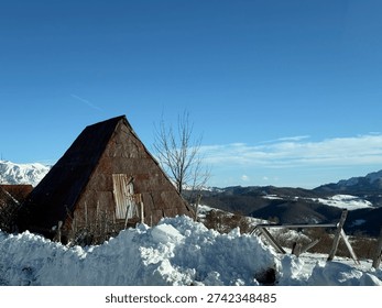 Rustic triangular barn in snow with mountain landscape under clear blue winter sky