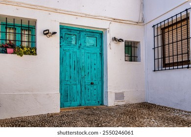 A rustic turquoise door stands out against a white stucco building, framed by small windows with iron bars - Powered by Shutterstock