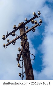 A rustic utility pole with aged ceramic insulators stands tall under a blue sky, highlighting the vintage infrastructure of an old communication system.