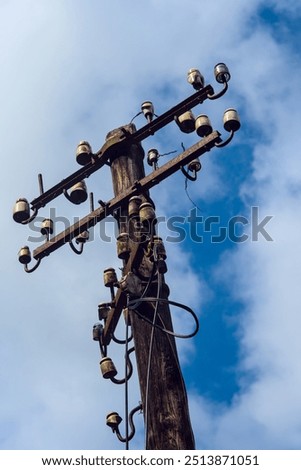 A rustic utility pole with aged ceramic insulators stands tall under a blue sky, highlighting the vintage infrastructure of an old communication system.