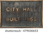 A rustic, weather worn sign indicating the location of City Hall and being built in 1855