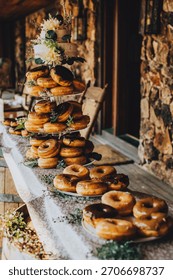Rustic wedding dessert display featuring stacked donuts with greenery and elegant décor in a warm reception setting.