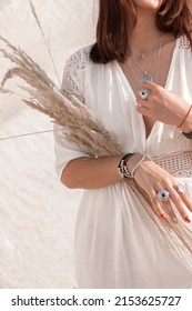 Rustic Wedding Details. Young Brunette Girl In White Boho Style Dress Stands Casual With Beige Dried Flower In Hands On The White Sand Career Background. Authentic Lifestyle Concept, Free Space