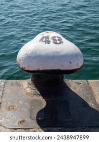 Rustic white bollard with the number 48, on a dock against blue water