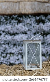 A Rustic White Lantern on Straw Against a Background of Beautiful Blossoming Flowers in Soft Focus, Perfect for Autumn or a Romantic Outdoor Setting to Highlight Nature's Beauty