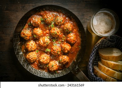 Rustic wholesome lunch of tasty savory meatballs in a spicy tomato and herb sauce served with a glass of beer and sliced baguette, close up overhead view